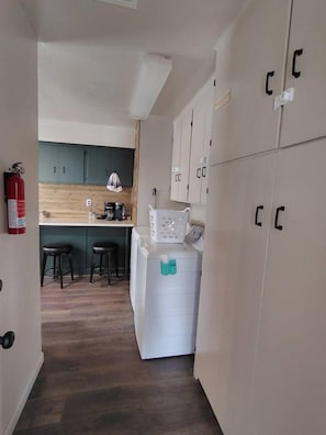 Un couloir étroit où se trouvent un lave-linge, une machine à café et un extincteur.