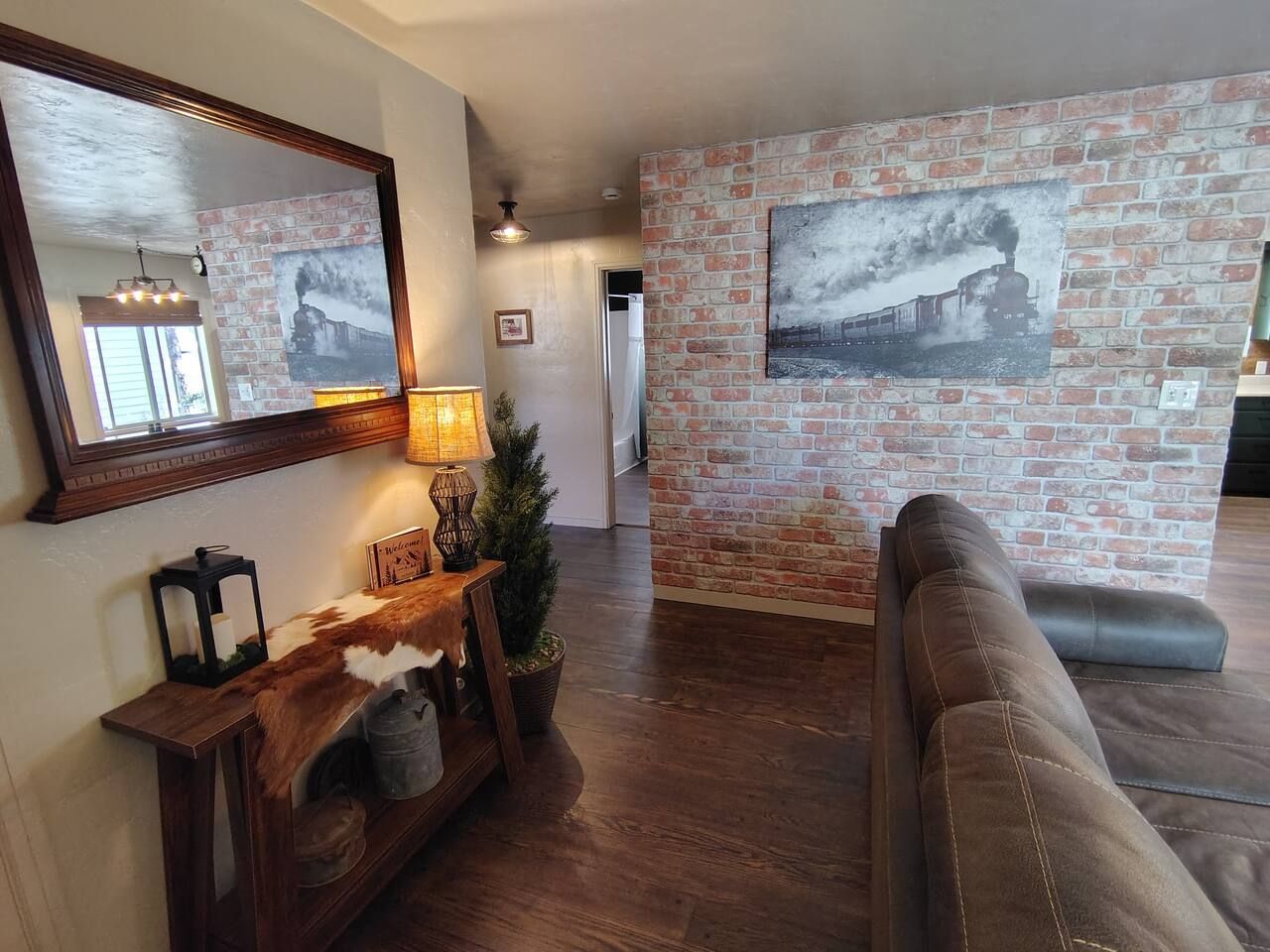 Una sala de estar con pared de ladrillo, un sofá, una consola de madera con objetos decorativos y una chimenea.