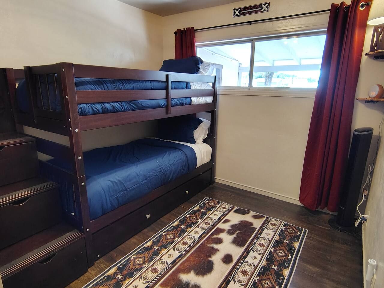 Una litera con ventana, una alfombra estampada y un estante pequeño.