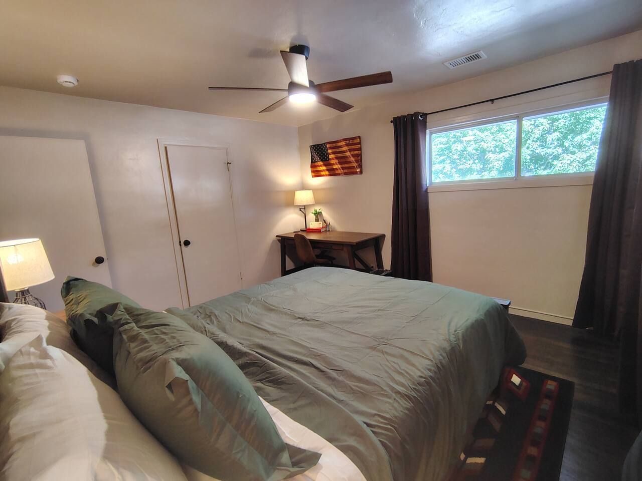 Een slaapkamer met een bed, een bureau, een lamp en een plafondventilator.