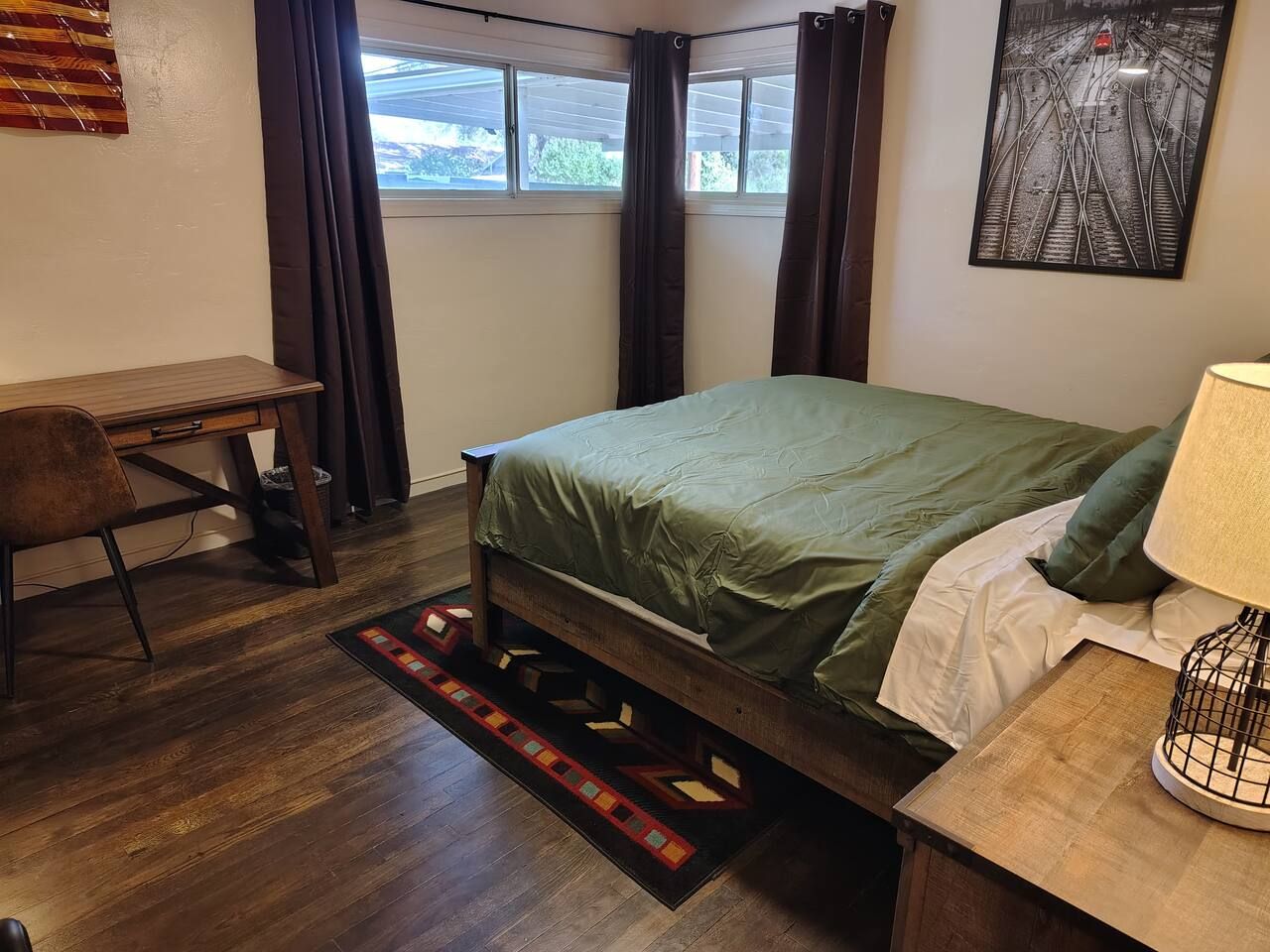 Une chambre à coucher avec un lit, un bureau, une chaise, une lampe et une fenêtre avec des rideaux.