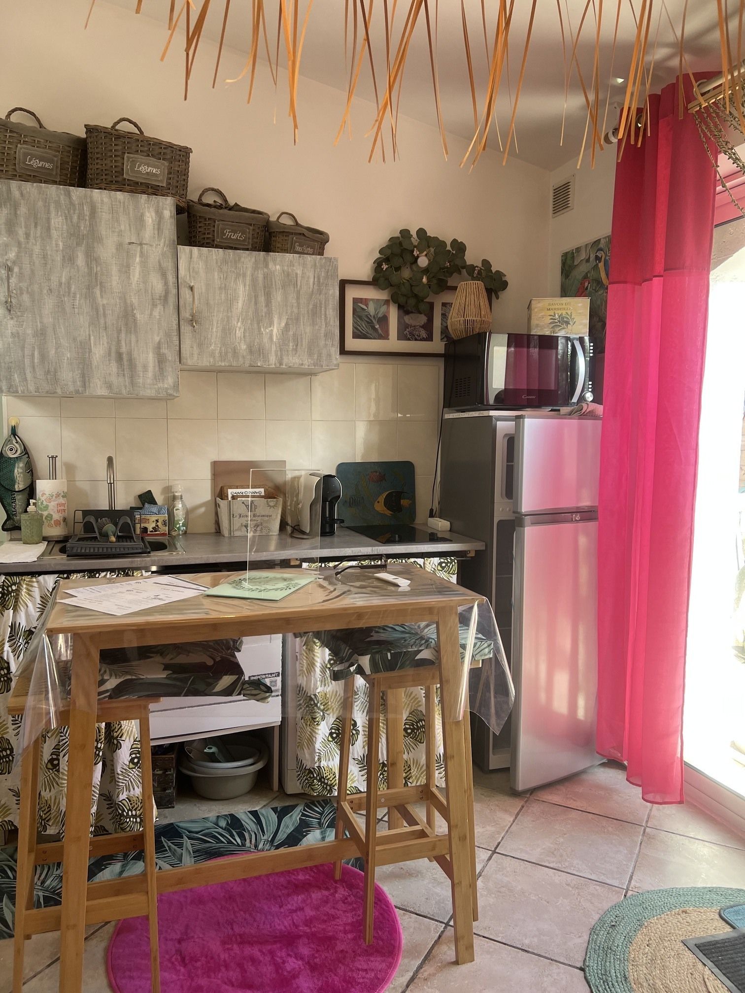 A kitchen with a refrigerator, a microwave, and a sink. There are baskets labeled 'Legumes' and 'Fruits' on the wall.