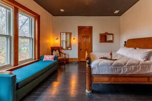 Un dormitorio con cama, un asiento junto a la ventana, una silla y una puerta.
