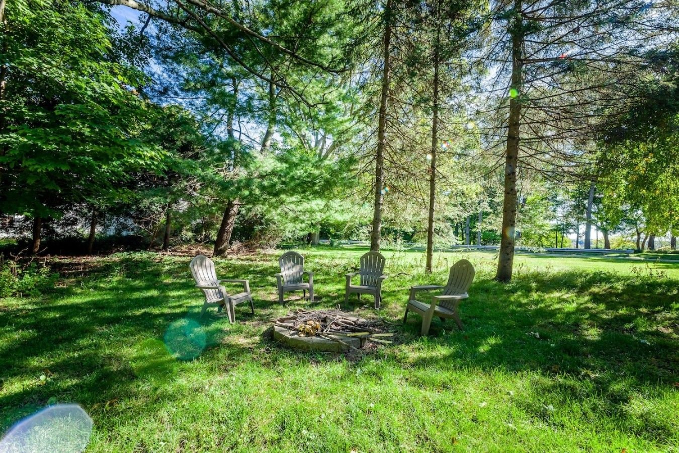 A grassy outdoor area with a fire pit and Adirondack chairs.