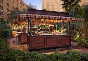 Un bar al aire libre con toldo a rayas, taburetes y una variedad de botellas.