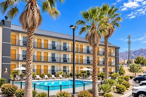 A multi-story hotel with a swimming pool, palm trees, and mountain views. - Top Town Extended Stay By Relianse (El Paso)