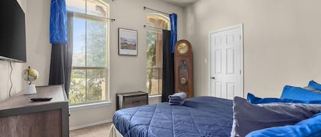 A bedroom with a bed, a desk, a television, a clock, and a window with curtains.