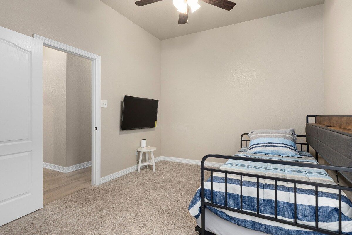 Une chambre à coucher comprenant un lit, un téléviseur, un ventilateur de plafond et une porte donnant sur une autre pièce.