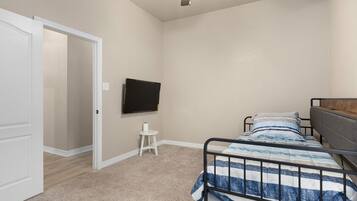 Une chambre à coucher comprenant un lit, un téléviseur, un ventilateur de plafond et une porte donnant sur une autre pièce.