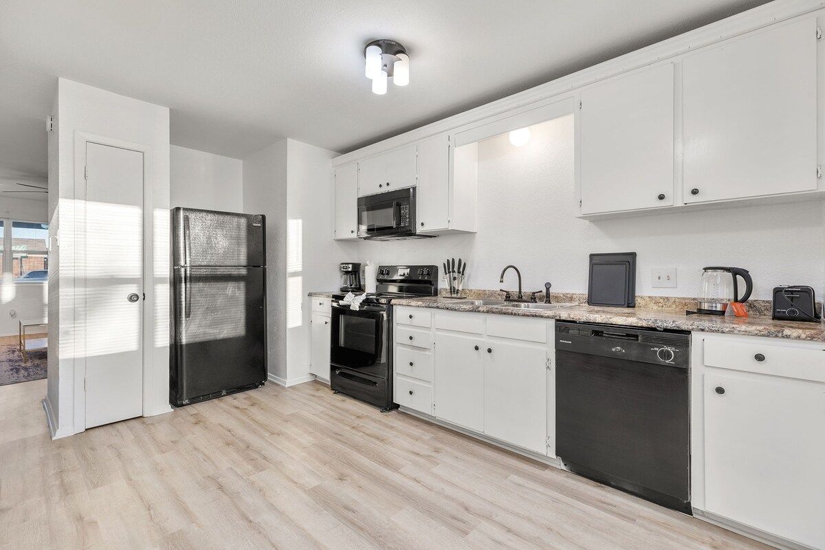 Una cocina moderna con armarios blancos, un refrigerador de acero inoxidable, un microondas, un horno y un lavavajillas.