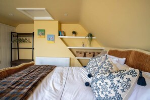 Quarto com cama, cabideiro, estantes com livros e plantas, e radiador.