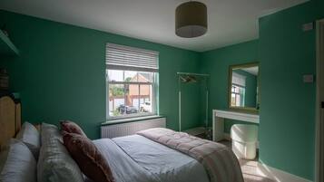 Ein Schlafzimmer mit einem Bett, einem Fenster, einer Heizung, einem Spiegel und einer weißen Mülltonne.