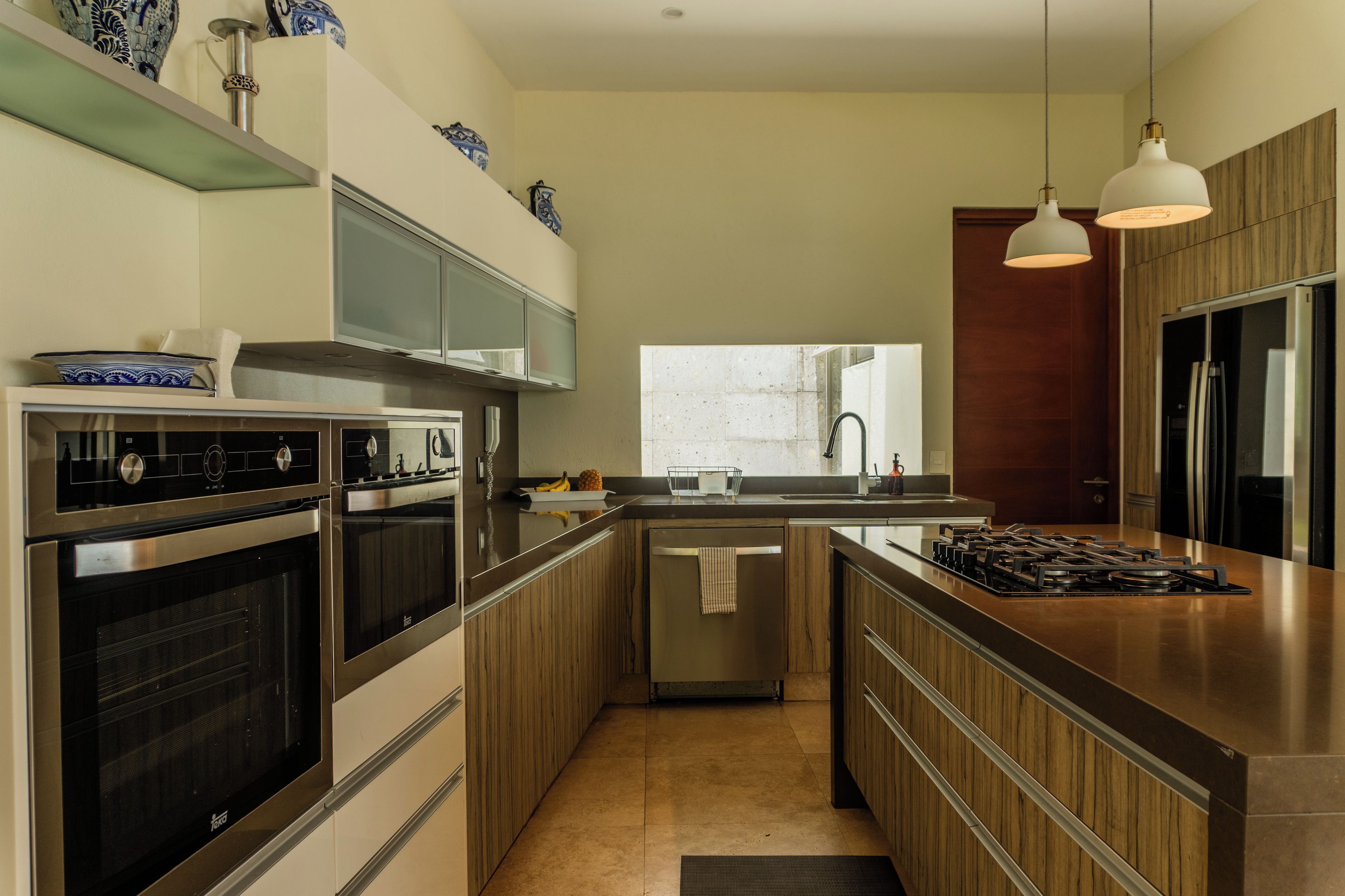 A modern kitchen with stainless steel appliances, wooden cabinets, and pendant lighting.