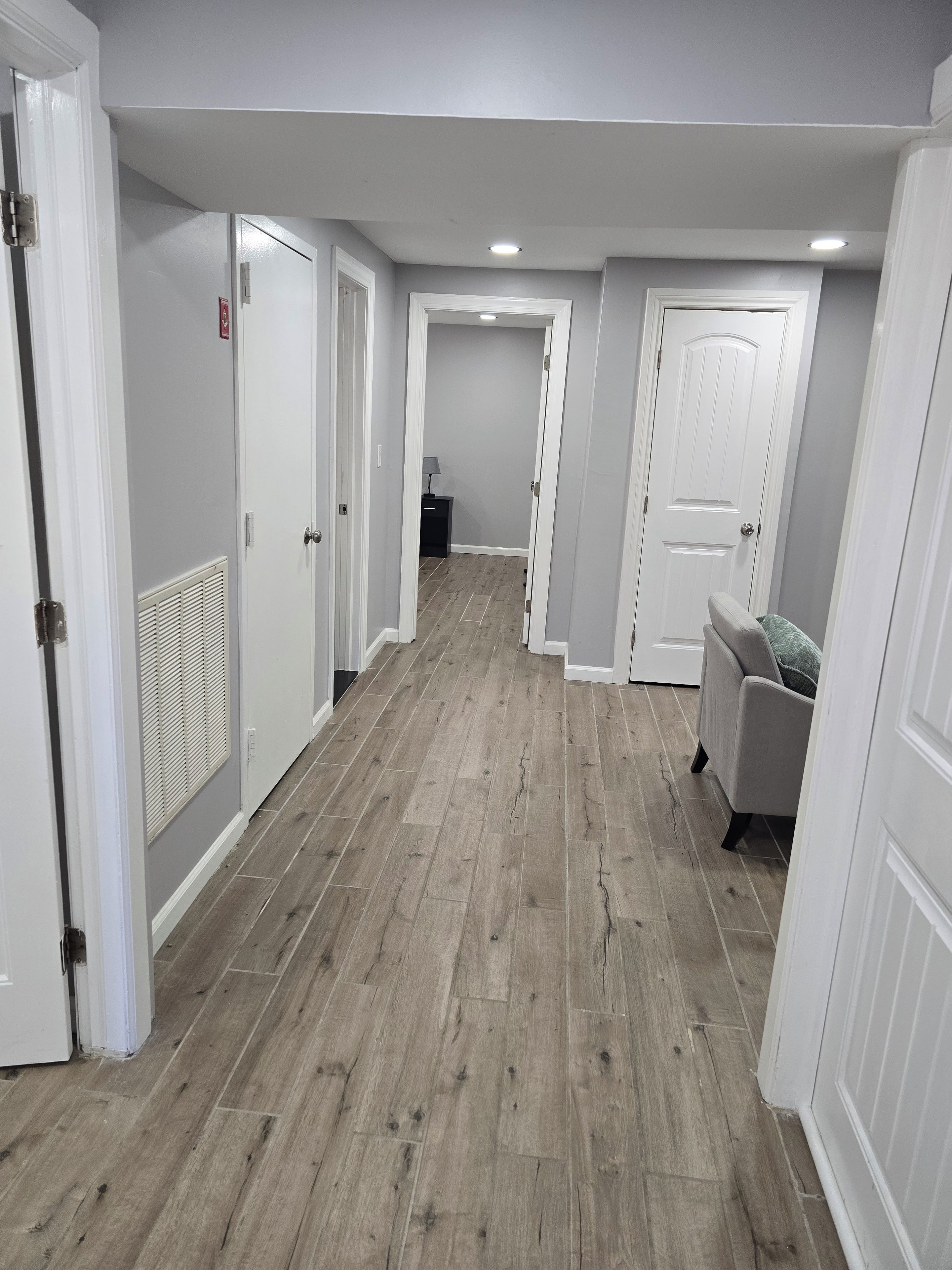 Un couloir doté d’un plancher en bois, de murs blancs et de portes donnant sur d’autres pièces.