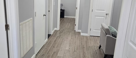 A hallway with wooden flooring, white walls, and doors leading to other rooms.