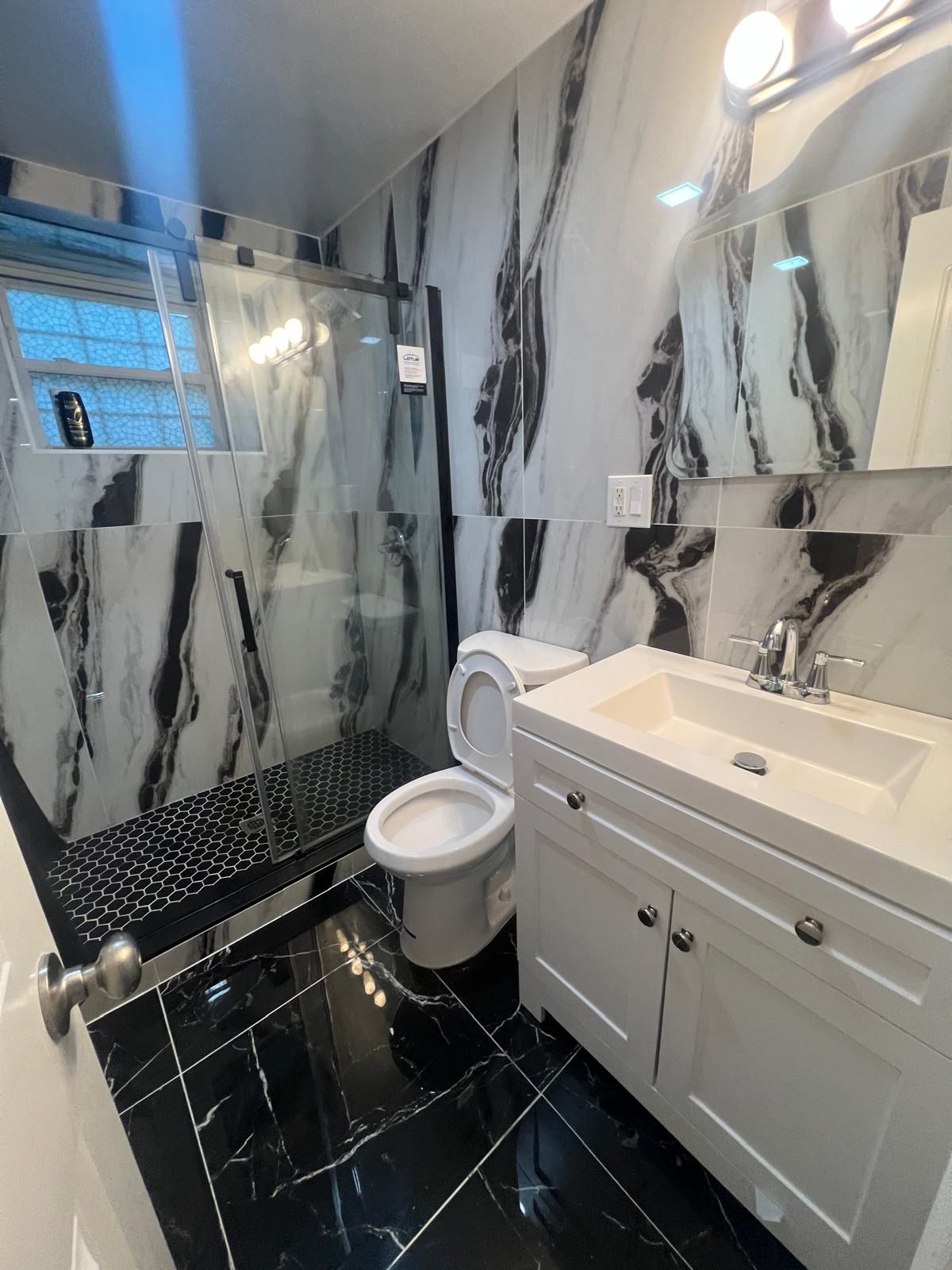 Une salle de bain moderne avec une douche à parois de verre, des toilettes, un lavabo avec un miroir et des murs à motifs de marbre.
