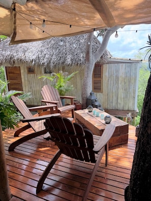 Una terraza exterior de madera con estructuras de techo de paja, mobiliario de madera y luces colgantes.