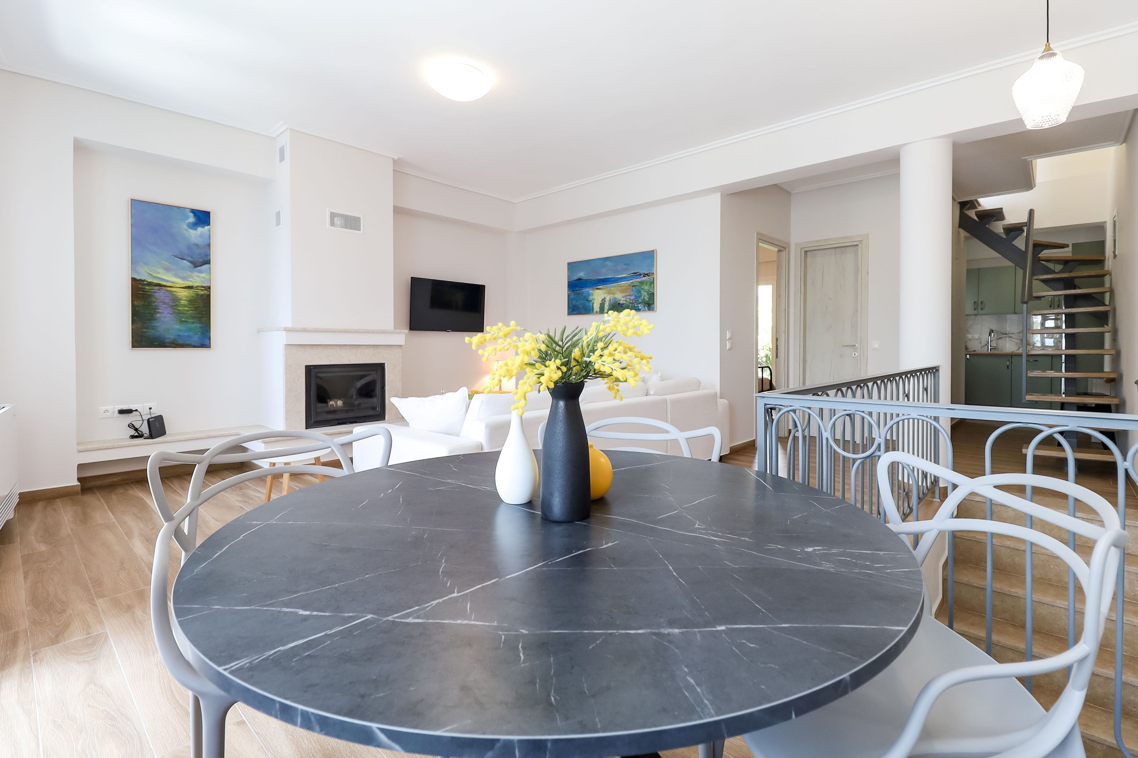 A modern living room with a round black table, white chairs, a fireplace, and artwork on the walls.