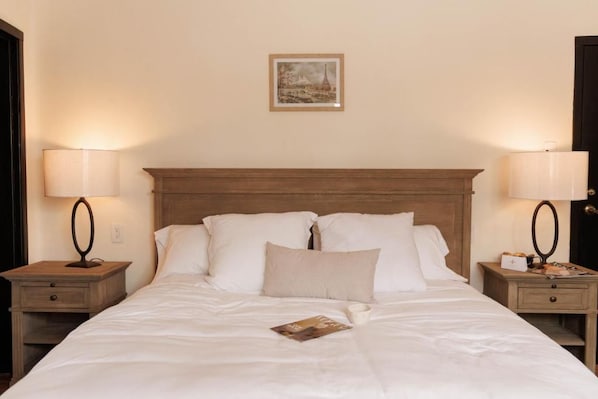 A neatly made bed with white linens, two bedside tables with lamps, and a framed picture on the wall.