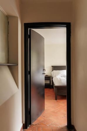 A narrow hallway leading to a bedroom with a bed and nightstand.
