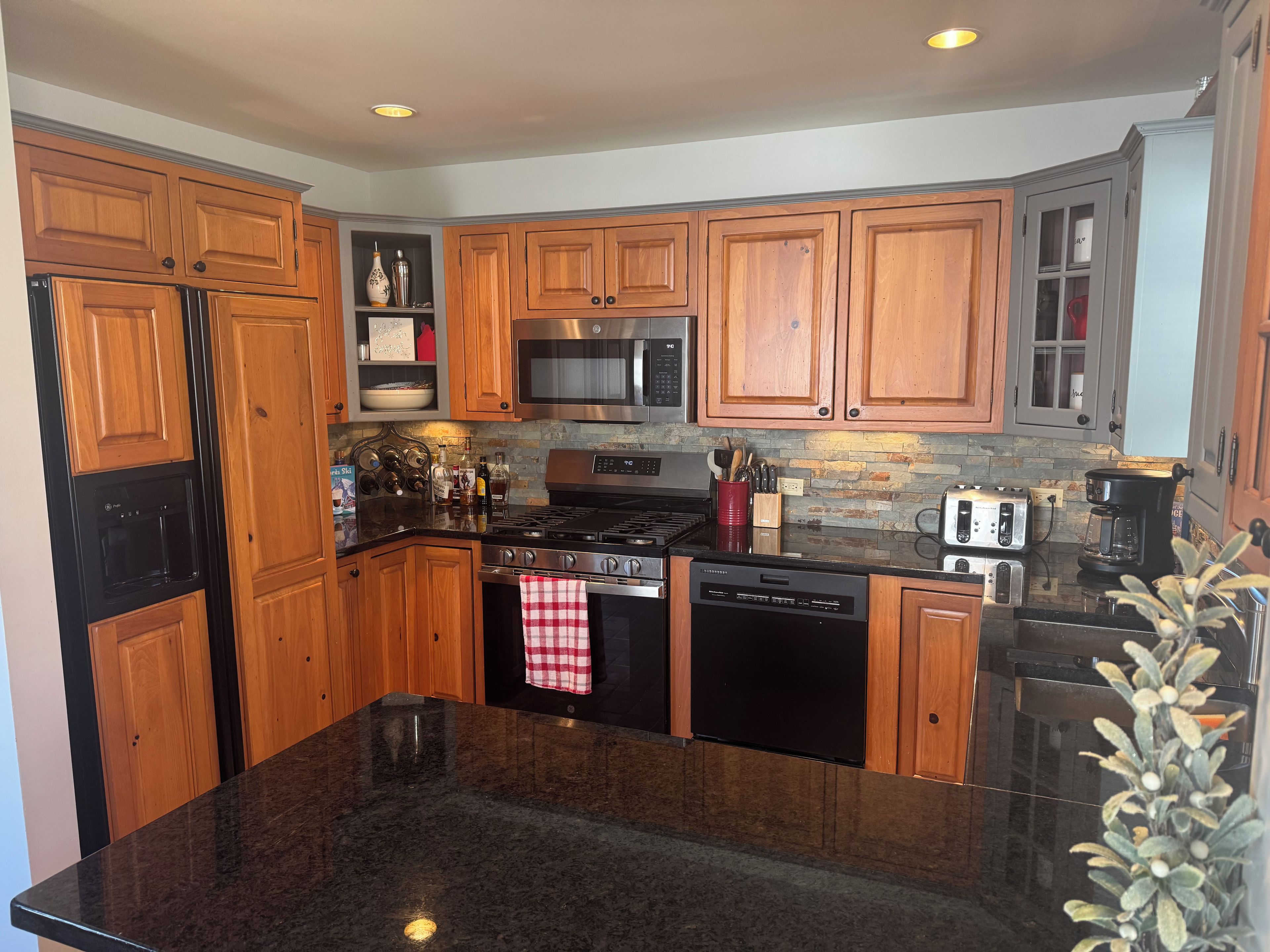 A kitchen with wooden cabinets, stainless steel appliances, a granite countertop, and a stone backsplash.