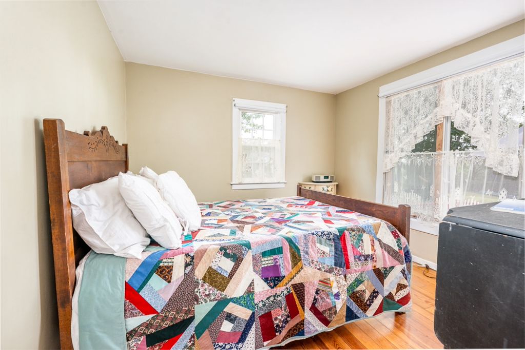 A bedroom with a wooden bed, a quilt, a window with a view, and a nightstand.
