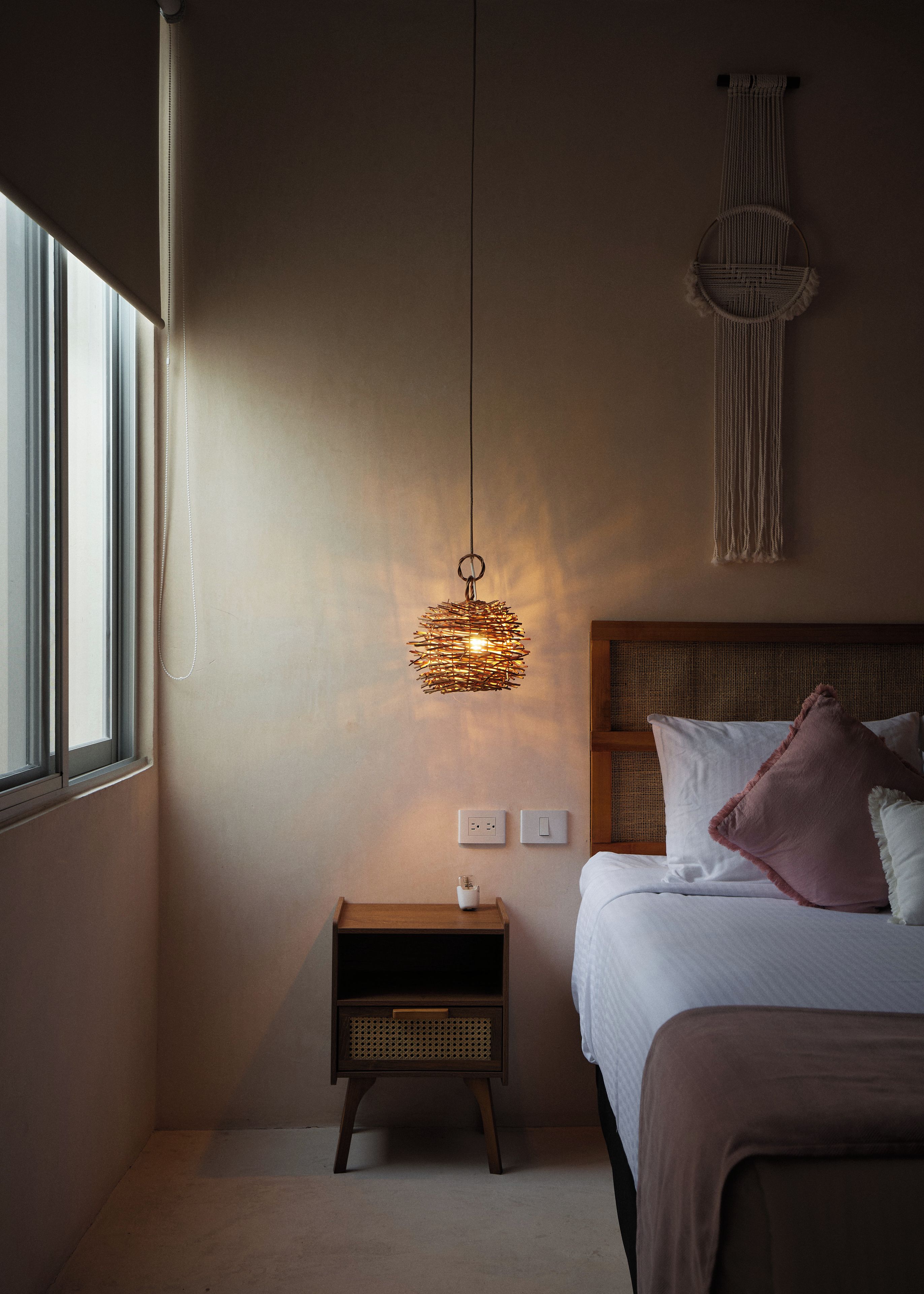 A bedroom with a bed, bedside table, wall-mounted light fixture, and a wall hanging.