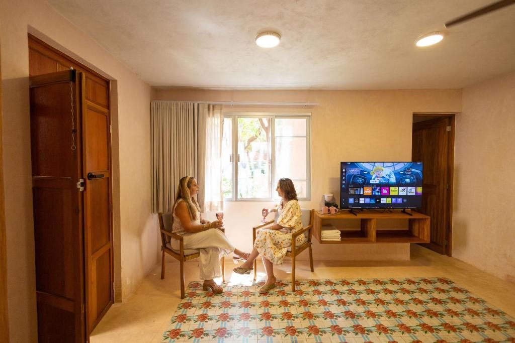 A room with a television, two chairs, a window with curtains, and a patterned carpet.