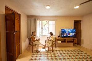 A room with a television, two chairs, a window with curtains, and a patterned carpet. - Casa Sofía Centro (Merida)