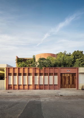 A building with a large, circular structure in the background, a gated entrance with a sign, and a paved area in the foreground. - Casa Sofía Centro (Merida)