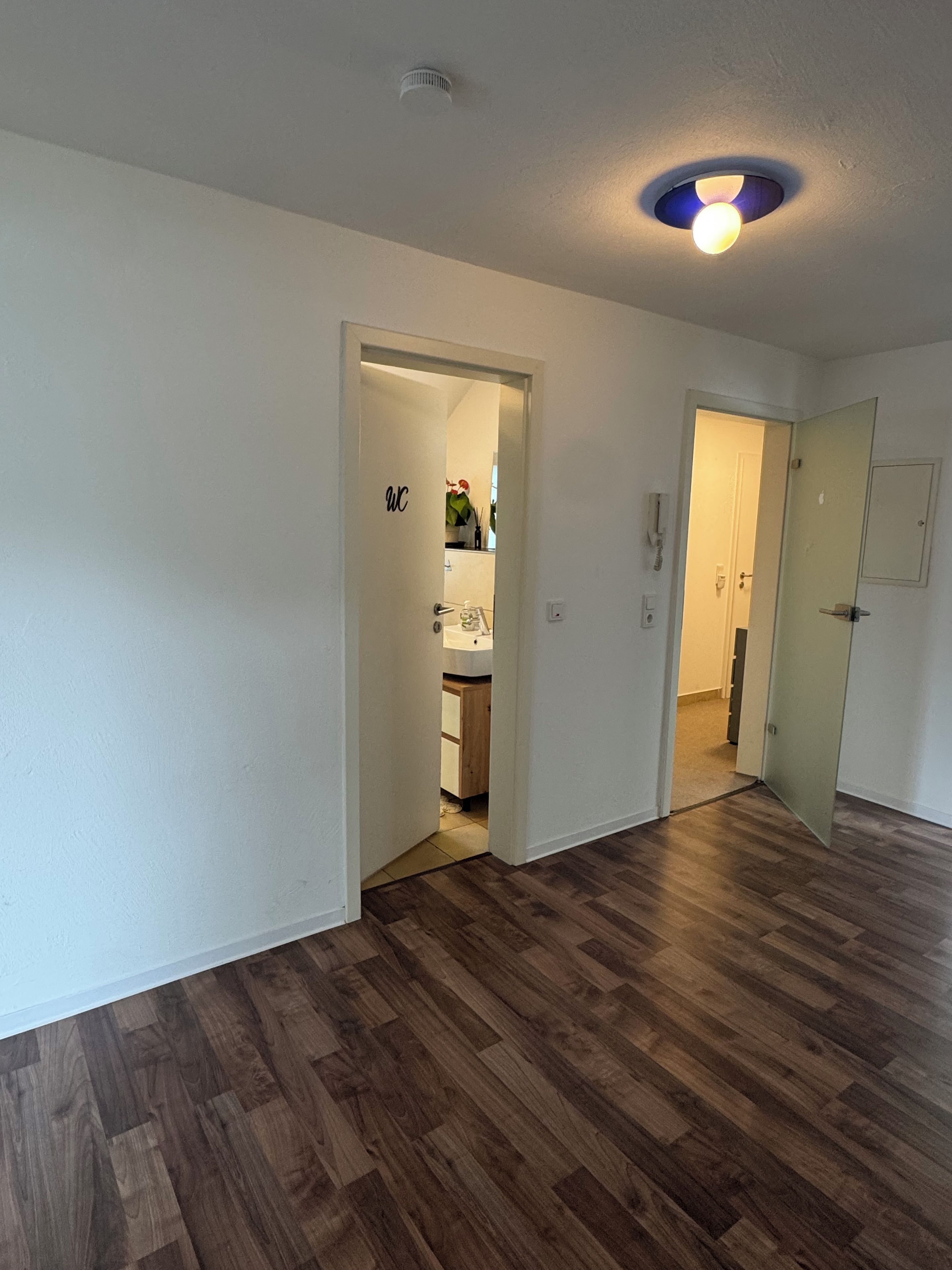 A room with wooden flooring, white walls, and a ceiling light fixture.