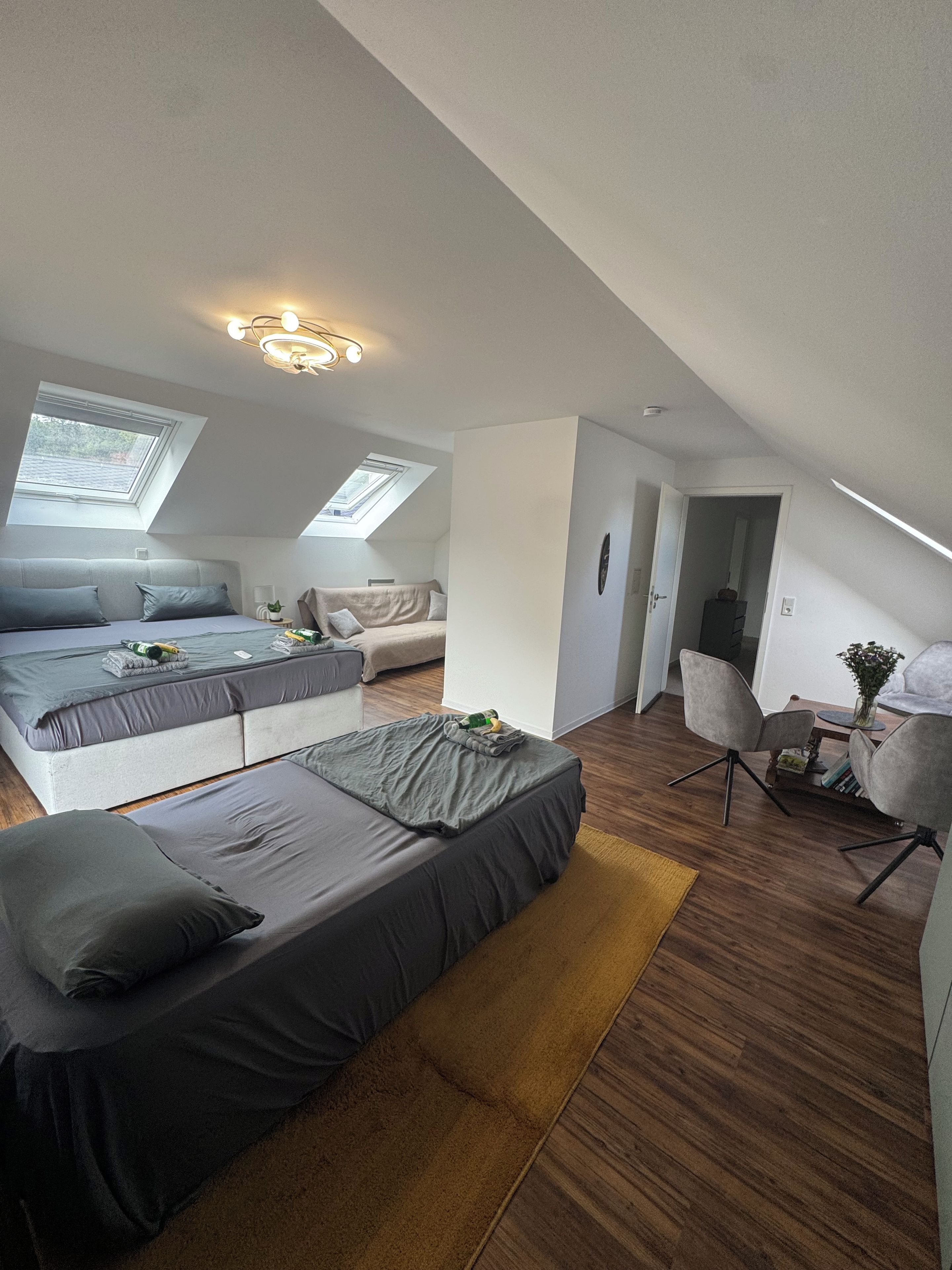 A modern loft bedroom with a skylight, a sofa bed, a dining area with a table and chairs, and a small kitchen area.