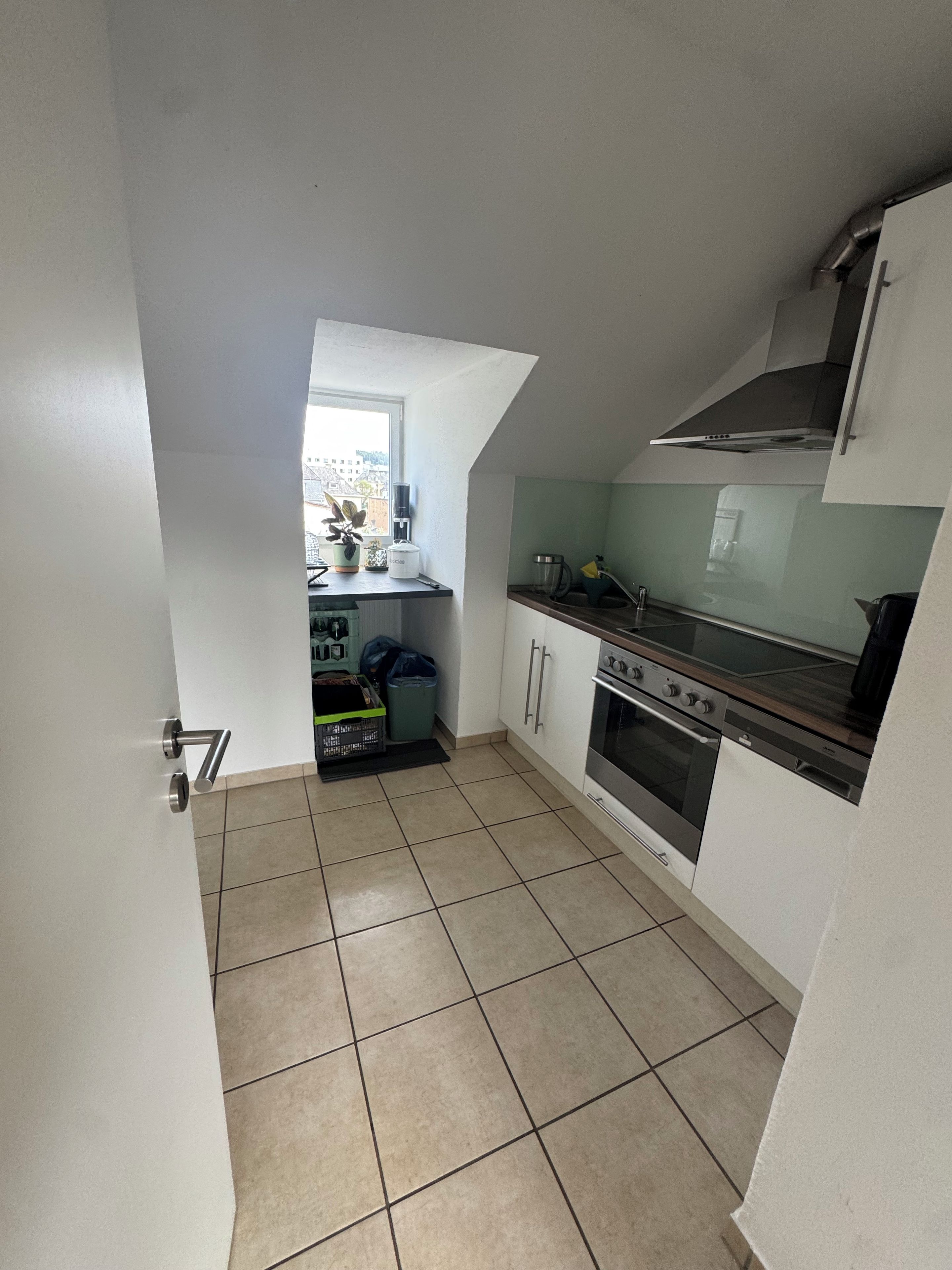 A compact kitchen with a gas stove, oven, and a window overlooking a cityscape.