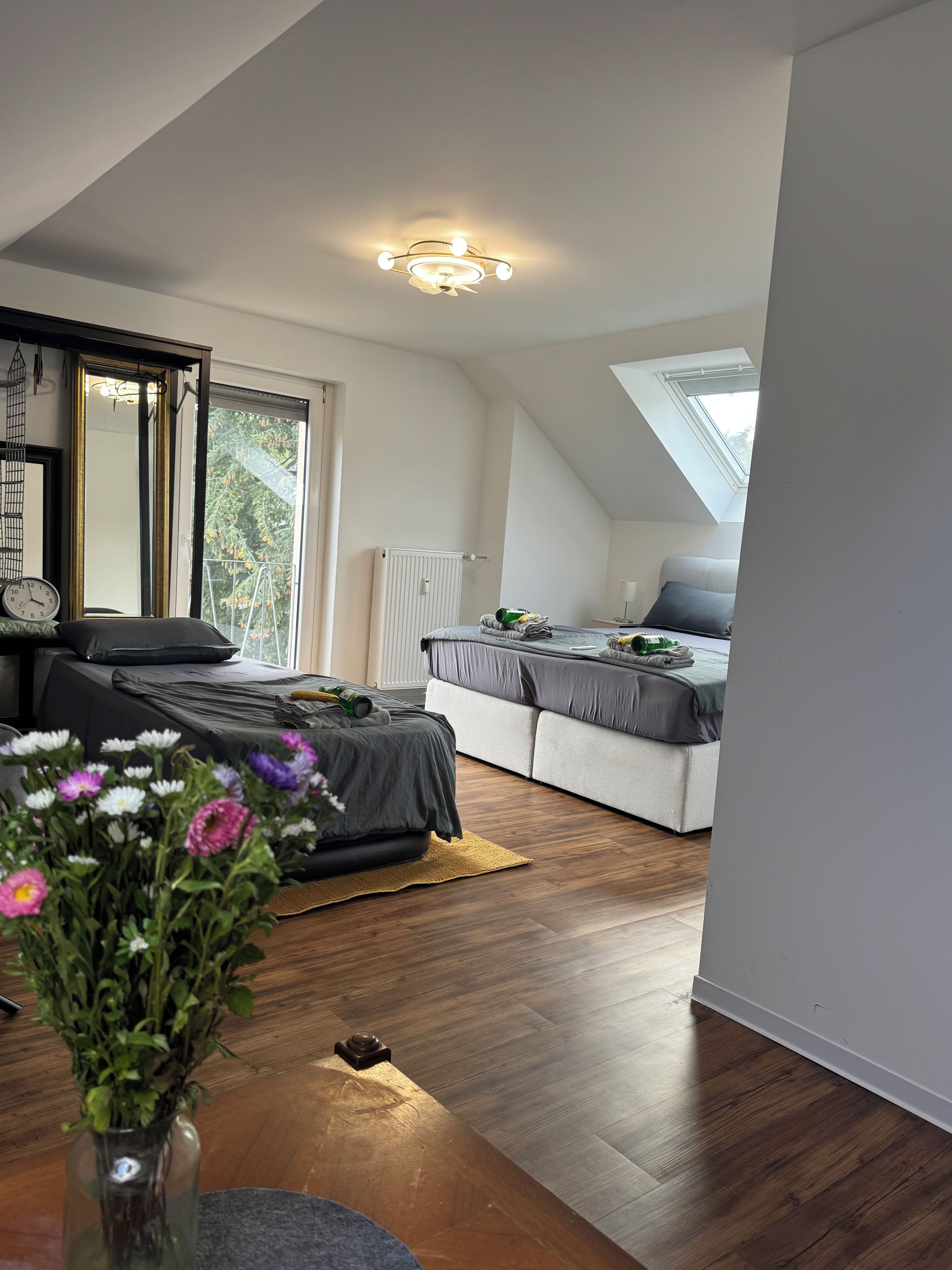 A modern bedroom with a skylight, a bed, a sofa, and a wooden floor.