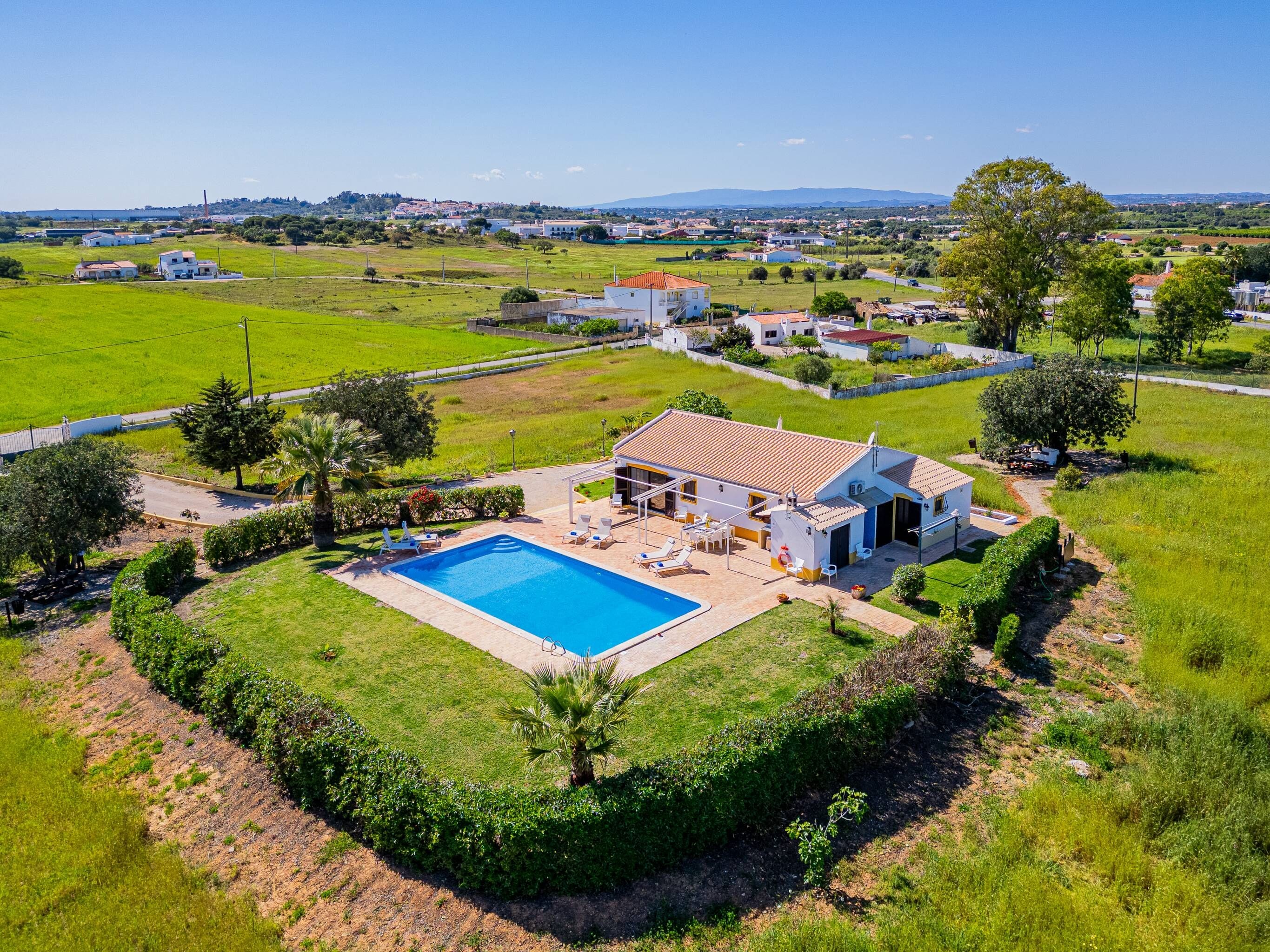 A residential property with a swimming pool, a patio with outdoor furniture, and a view of a green landscape.