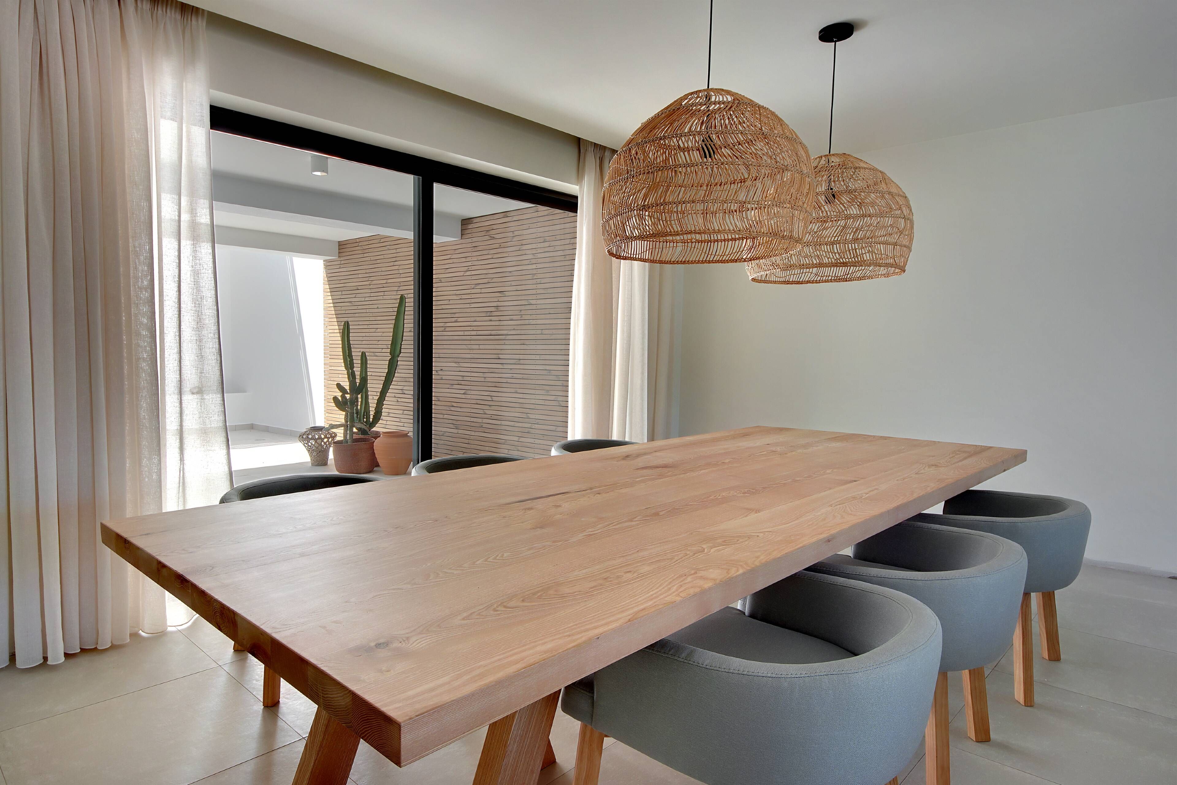 A modern dining area with a wooden table, grey upholstered chairs, and a woven pendant light.