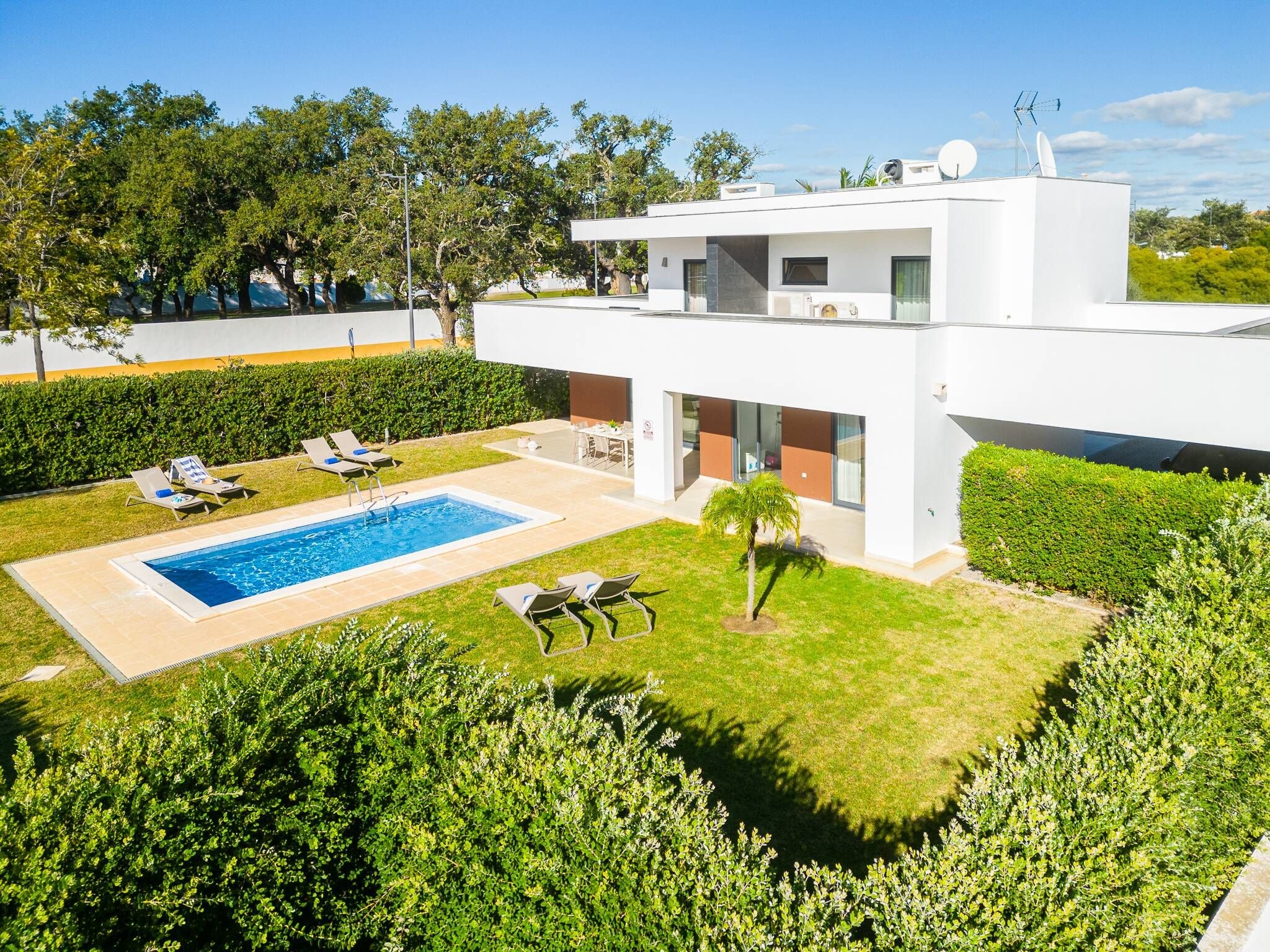 A modern two-story house with a swimming pool, lounge chairs, and a well-maintained garden.