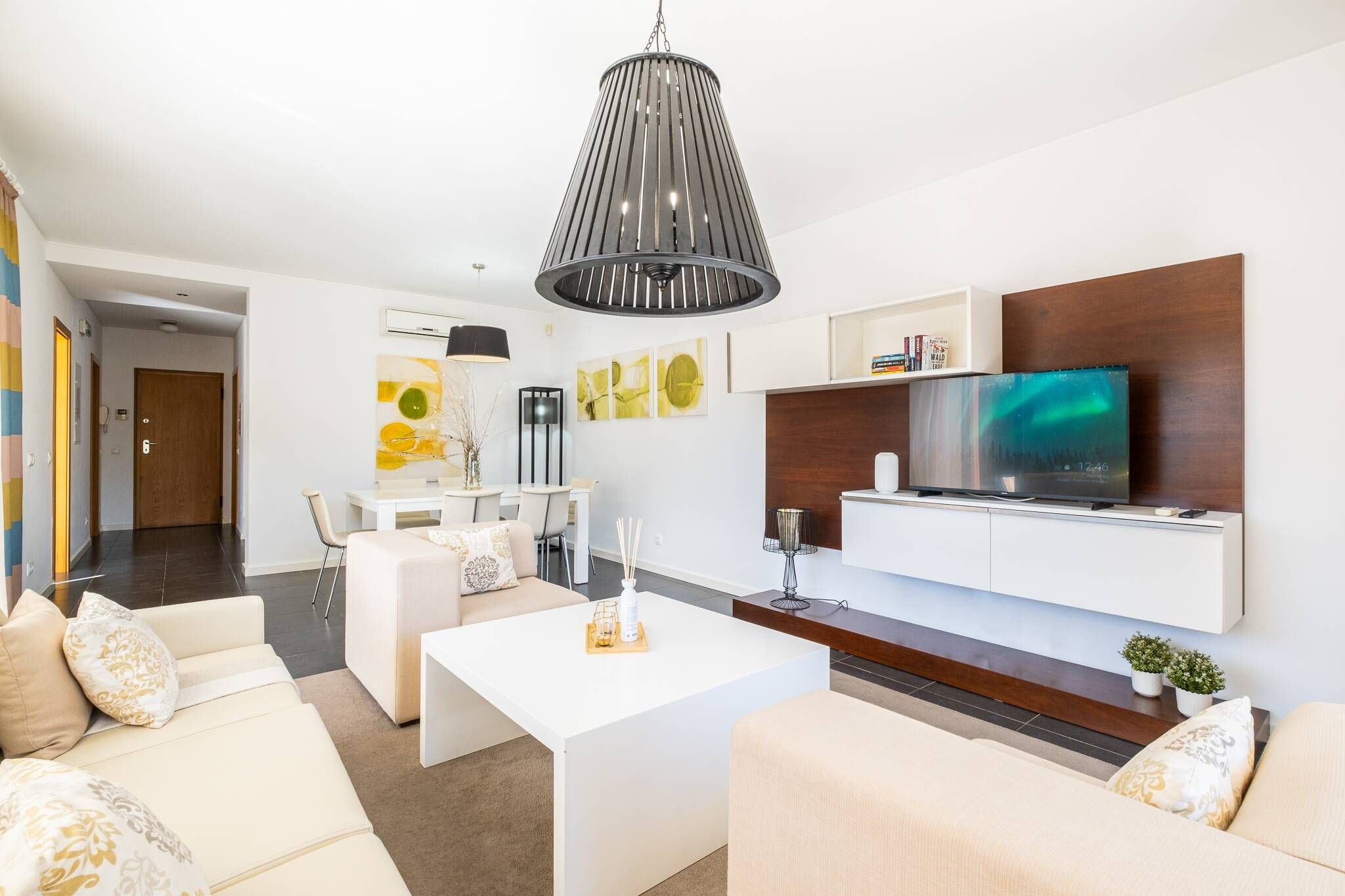 A modern living room with a flat-screen TV, white sofas, a coffee table, and a pendant light.