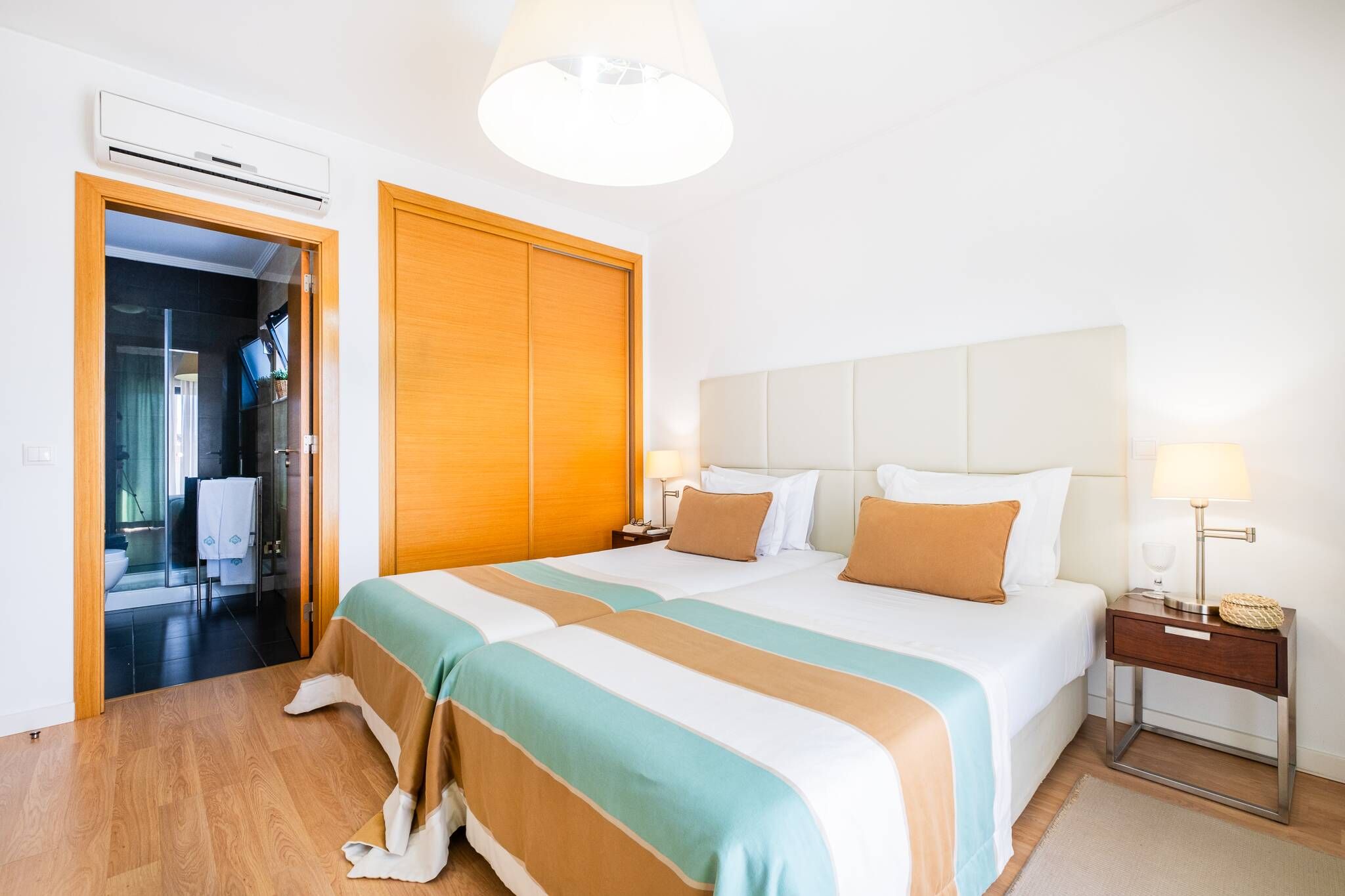 A hotel room with a bed, bedside tables, a lamp, and an air conditioning unit.