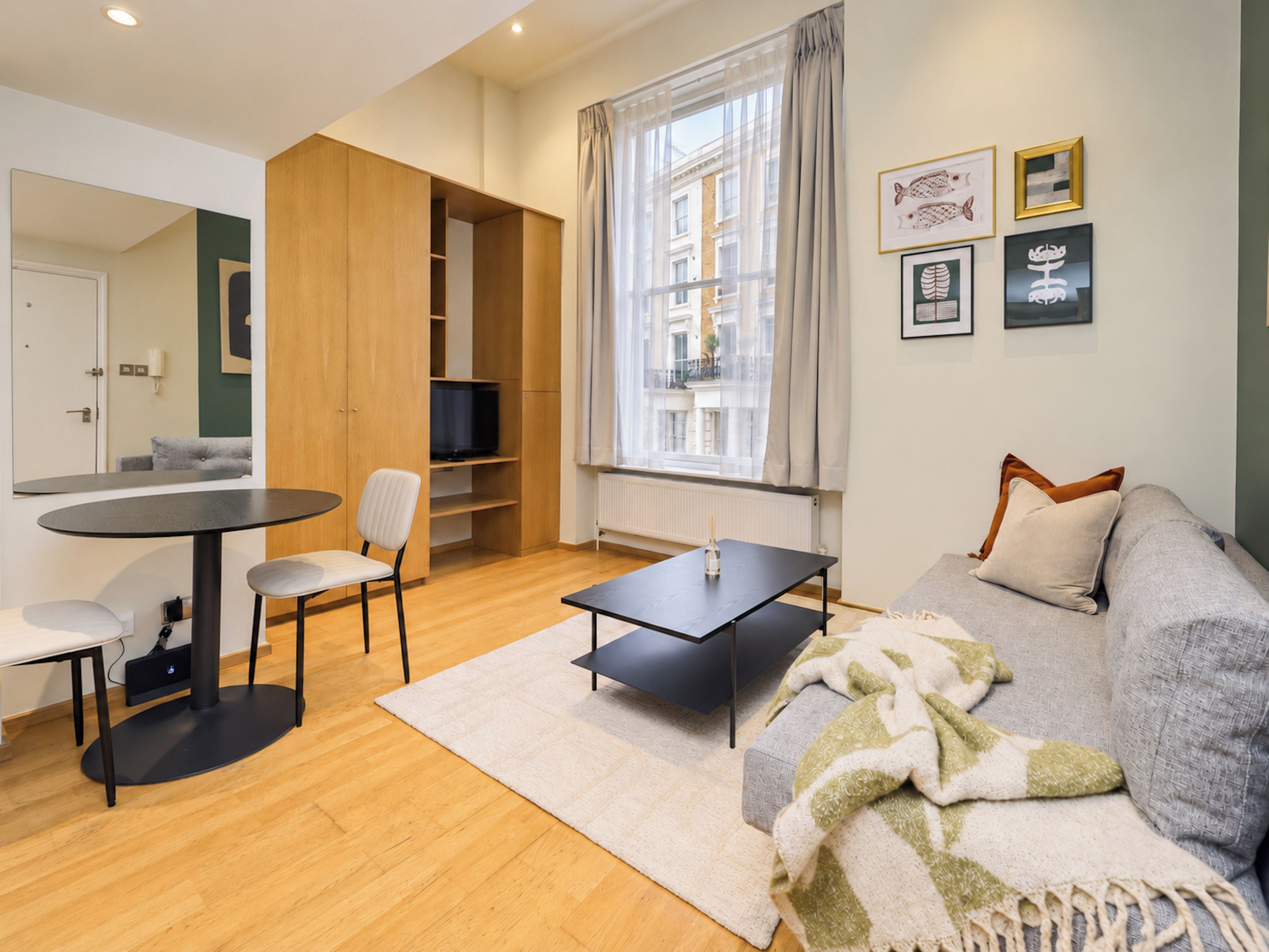 Una sala moderna con sofá, una mesa de centro, televisor y un área de comedor con mesa y sillas.