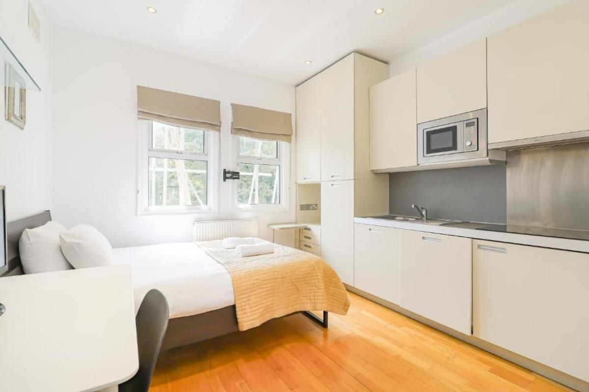 Ein modernes Hotelzimmer mit Bett, Schreibtisch, einer Küchenzeile und großen Fenstern.