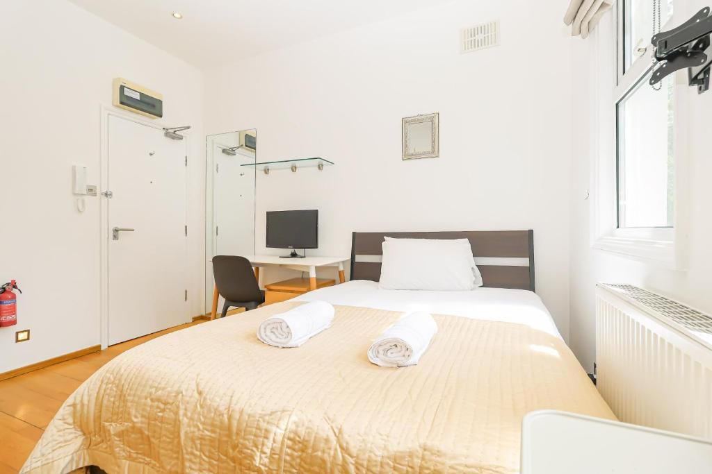 Habitación de hotel con cama, escritorio con computadora, silla, televisor y ventana.