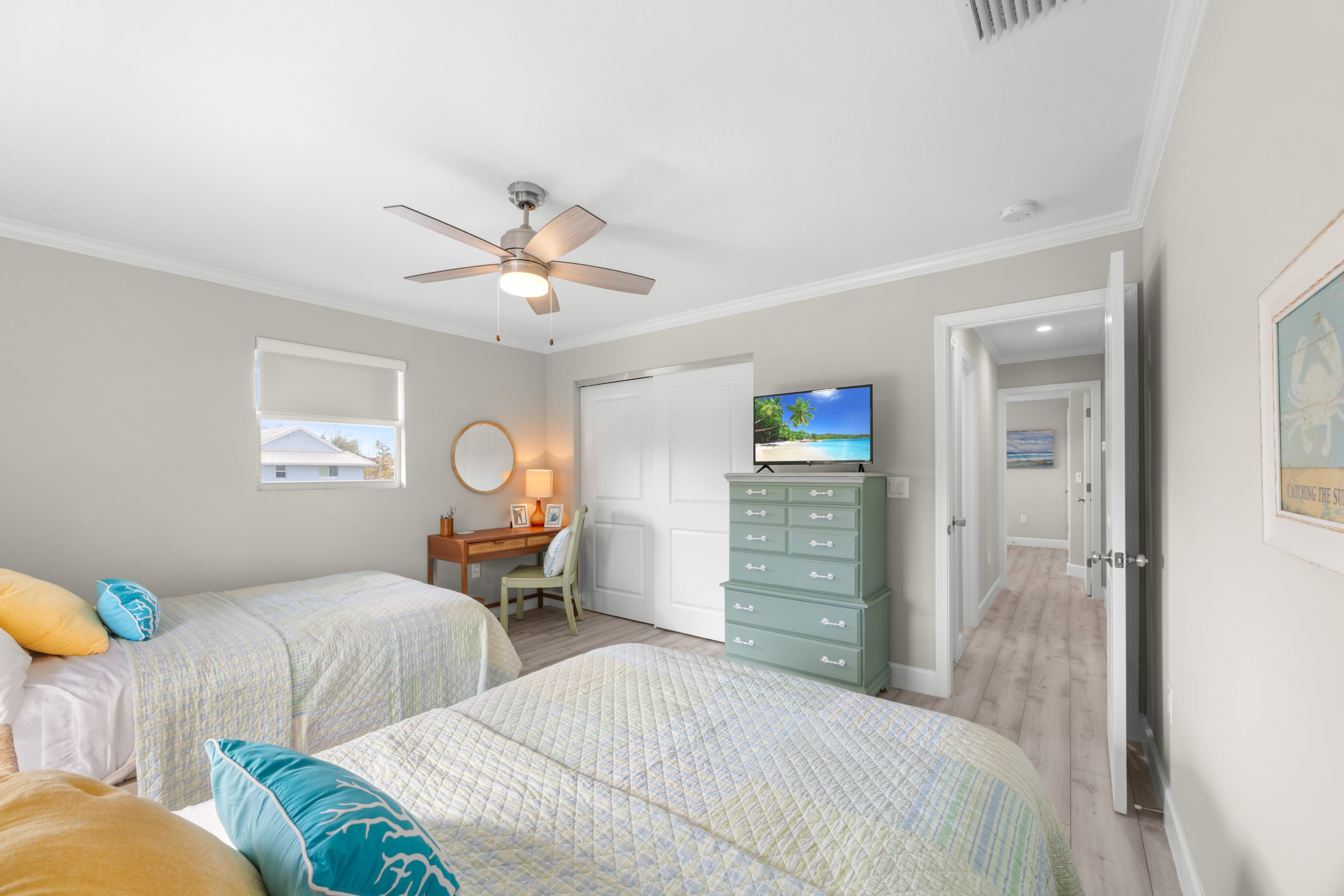 Une chambre avec deux lits, un bureau, une commode, un ventilateur de plafond et un téléviseur.