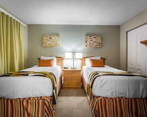 Una habitación de hotel con dos camas, una mesita de noche con una lámpara y dos obras de arte colgadas en la pared.