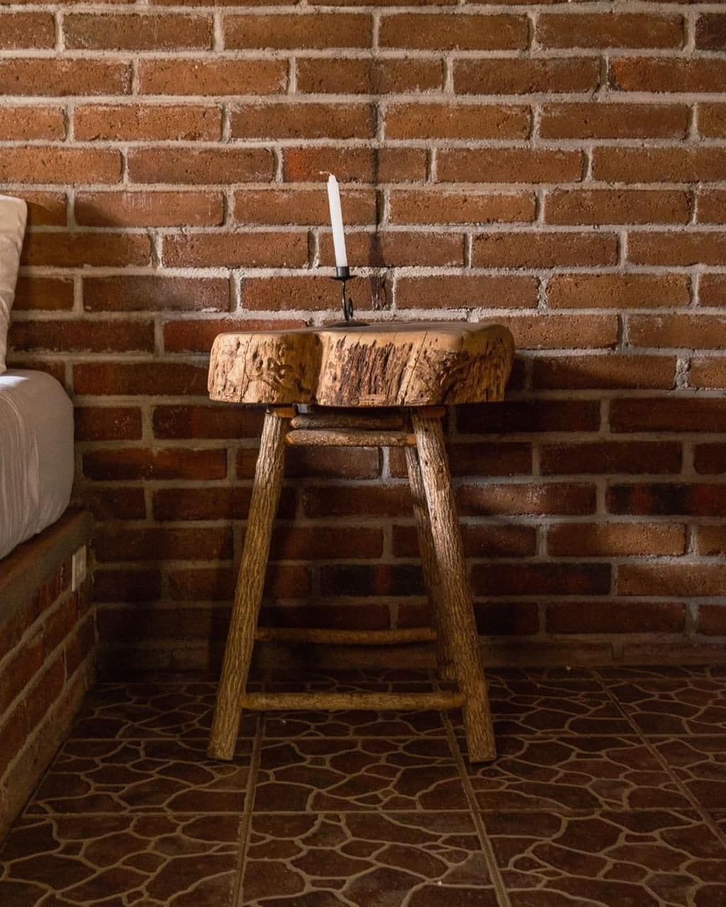 A rustic wooden stool with a candle holder, placed against a brick wall.