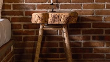 A rustic wooden stool with a candle holder, placed against a brick wall.