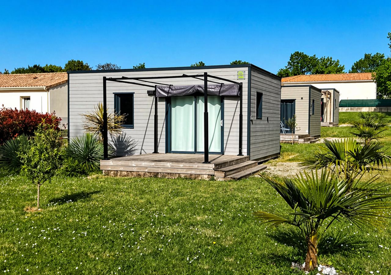 Une maison mobile moderne dotée d’un patio couvert, entourée d’une pelouse bien entretenue et de petits arbres.