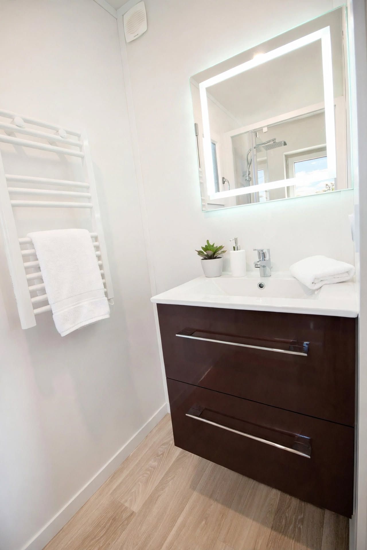 Une salle de bain moderne avec un meuble-lavabo blanc, un miroir, un porte-serviettes et une petite plante en pot.