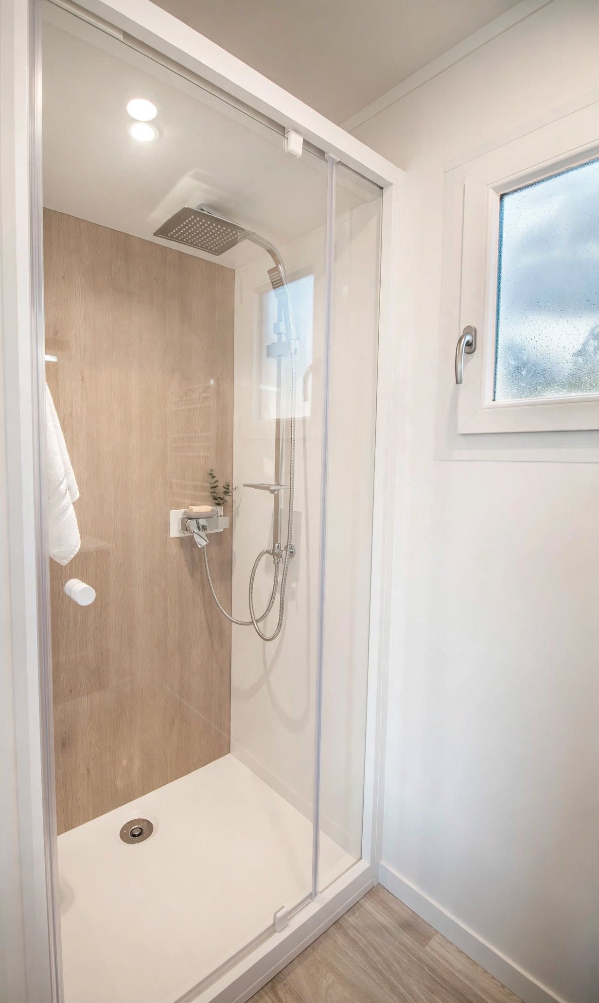 Un espace douche entièrement vitré, avec un mur en bois, un sol blanc et une fenêtre donnant sur un paysage agréable.