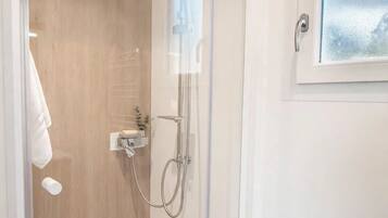 Un espace douche entièrement vitré, avec un mur en bois, un sol blanc et une fenêtre donnant sur un paysage agréable.